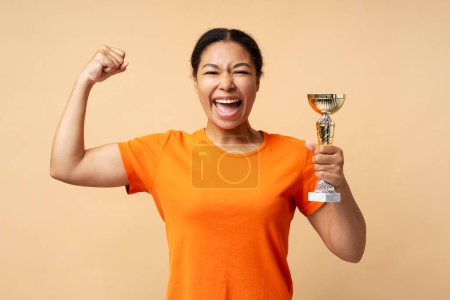 Photo for Young overjoyed African American woman holding trophy cup, celebration success isolated on beige background. Sport victory, winning competition concept - Royalty Free Image