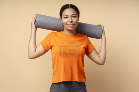 Photo for African American happy smiling woman 30s, with muscular strong aesthetic body looking confidently at camera, holding fitness yoga mat, isolated on blue background - Royalty Free Image