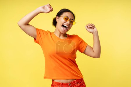 Photo for Portrait of beautiful smiling African American woman wearing orange t shirt dancing isolated on yellow background. Smiling stylish fashion model having fun. Summer concept - Royalty Free Image