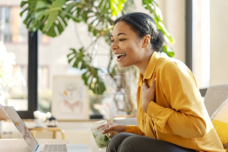Téléchargez les photos : Femme d'affaires afro-américaine souriante moderne, pigiste ayant un appel vidéo sur ordinateur portable, travaillant en ligne depuis la maison. Femme élégante assise dans un café. Une entreprise prospère - en image libre de droit