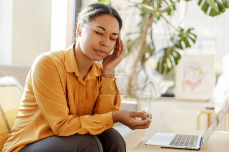 Téléchargez les photos : Femme d'affaires afro-américaine fatiguée frotter les yeux tout en travaillant ordinateur portable en ligne de la maison. Femme élégante assise dans un café. Une entreprise prospère - en image libre de droit