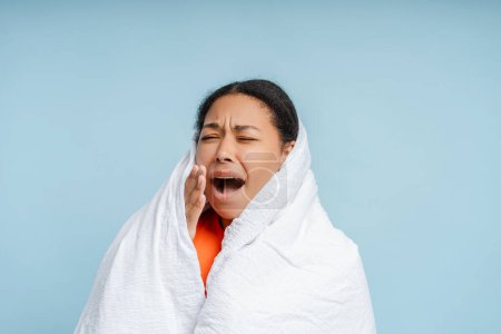 Photo for Yawning woman relaxing at home wrapped in soft blanket, feeling tired isolated on blue background studio portrait. Bad nap concept - Royalty Free Image