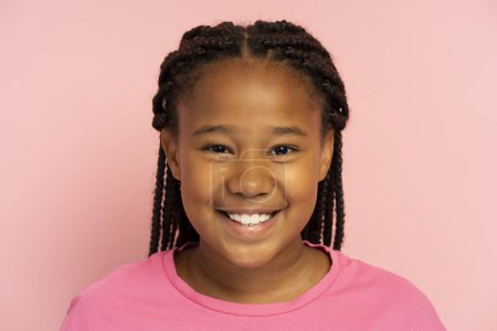 Photo for Portrait of cute smiling African American girl wearing stylish hairstyle, dreadlocks, pigtails wearing casual pink t shirt standing isolated on pink background, looking at camera, closeup - Royalty Free Image