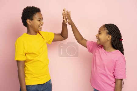 Photo for Smiling African American kids wearing colorful t shirts giving high five isolated on pink background - Royalty Free Image