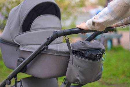 Photo for Close-up of a stylish modern baby waterproof and windproof eco-leather stroller in gray color and mom's hands pushing the pram during outdoor recreation. Buggy. Baby carriage. Pushchair - Royalty Free Image