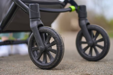 Photo for Details on black wheels of a baby carriage on the background of asphalt. Closeup wheels go on the road with copy space for advertising text. Baby transport. Newborn. Stroller. - Royalty Free Image
