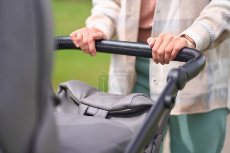 Photo for Details on the hands of an unrecognizable mother pushing stylish baby stroller of gray color while walking outdoors. Waterproof and windproof newborn carriage from eco leather. Baby transport. Buggy - Royalty Free Image