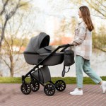 Young woman pushing stroller, walking outdoors in park. Smiling, happy mother with baby in carriage
