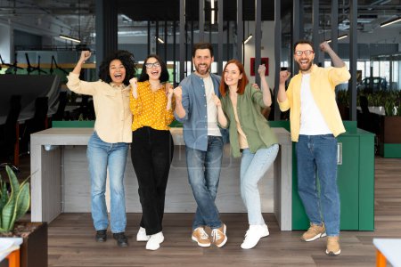 Photo for Successful team of diverse business partners colleagues clenching fists from excitement, smiling looking at camera, standing in modern corporate office interior. People. Teamwork. Career - Royalty Free Image