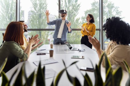Inspired Caucasian young man wearing VR goggles, playing virtual reality online games during team building training in modern office interior. People. Career. Professional and personal growth.
