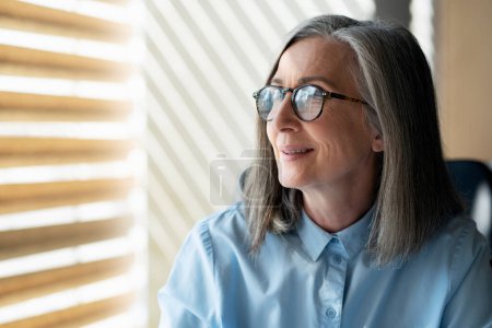 Photo for Portrait of smiling senior businesswoman looking at window in modern office. Successful business - Royalty Free Image