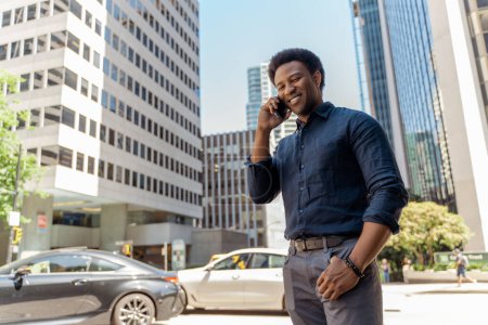 Foto de Retrato del hombre afroamericano confiado hablando por teléfono móvil, respondiendo a una llamada mirando hacia otro lado en la calle de la ciudad. Gerente de éxito, empleado, empresario - Imagen libre de derechos