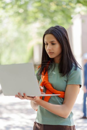 Photo for Smart, pensive student using laptop, learning languages on street. Female freelancer, online work, online shopping. Online education concept - Royalty Free Image
