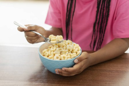 Photo for African American child, girl sitting at desk holding spoon with cereal, having breakfast at home, selective focus, closeup. Concept of morning, cooking breakfast - Royalty Free Image