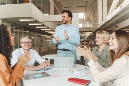 Photo for Group of smiling successful business people, managers sitting at desk in modern office, clapping their colleague for good job, working together. Teamwork, meeting, seminar, successful business - Royalty Free Image