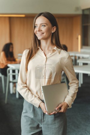 Photo for Attractive, good looking young businesswoman holding laptop working in modern office, looking away. Smiling businesswoman, successful entrepreneur. Business concept - Royalty Free Image