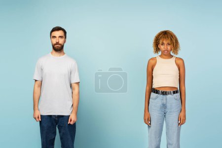Téléchargez les photos : Portrait de sérieux multiracial divers homme caucasien et femme afro-américaine en tenue décontractée regardant la caméra isolée sur fond bleu - en image libre de droit