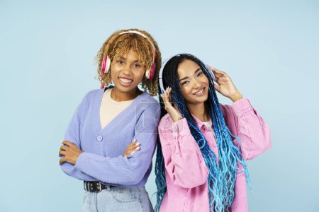 Foto de Mujeres afroamericanas sonrientes positivas que usan auriculares escuchando música mirando a la cámara aislada sobre fondo azul. Concepto Hobby - Imagen libre de derechos