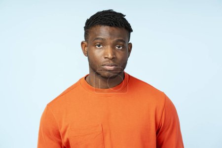 Téléchargez les photos : Sérieux, cher homme afro-américain attrayant debout isolé sur fond bleu en t-shirt orange regardant la caméra, posant en studio - en image libre de droit
