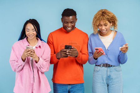 Téléchargez les photos : Groupe de souriants amis afro-américains élégants tenant des téléphones mobiles, en utilisant l'application moderne, la communication, le shopping en ligne isolé sur fond bleu. Technologie - en image libre de droit