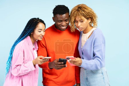 Foto de Grupo de elegantes amigos afroamericanos sonrientes sosteniendo teléfonos móviles, viendo videos, compras en línea, comunicación, aislados en un fondo azul. Tecnología, concepto de redes sociales - Imagen libre de derechos