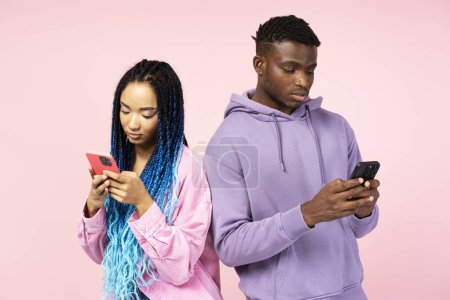 Téléchargez les photos : Couple d'amis afro-américains sérieux tenant des téléphones mobiles, la communication en ligne isolé sur fond rose. Technologie, concept de dépendance aux médias sociaux - en image libre de droit