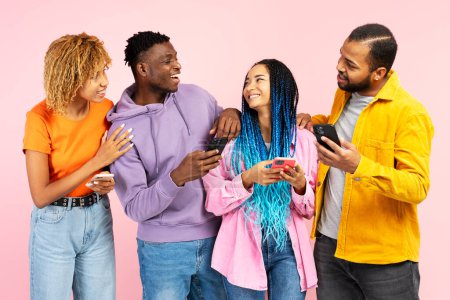 Photo for Group of attractive smiling African American friends holding mobile phones, communication, talking isolated on pink background. Technology, friendship concept - Royalty Free Image