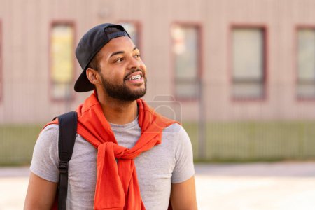 Téléchargez les photos : Portrait d'homme afro-américain souriant avec des appareils dentaires portant des vêtements décontractés élégants regardant loin debout dans la rue, espace de copie. Concept de publicité - en image libre de droit