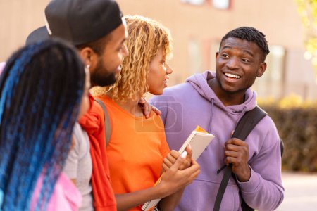 Téléchargez les photos : Groupe d'étudiants afro-américains souriants et élégants avec des sacs à dos, tenant des livres parlant, marchant sur le campus universitaire. Portrait d'amis heureux se rencontrant, se regardant dans la rue. Éducation - en image libre de droit