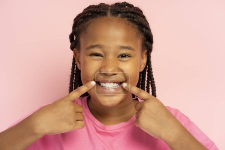 Téléchargez les photos : Petite afro-américaine souriante montrant ses dents blanches isolées sur fond rose - en image libre de droit