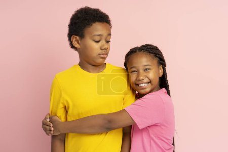 Photo for Portrait of smiling African American boy and girl, brother and sister wearing colorful t shirt hugging, looking at camera isolated on pink background. Concept of family, happy childhood - Royalty Free Image