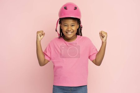 Foto de Retrato de una chica sonriente con una camiseta rosa casual y un casco de seguridad rosa mirando a la cámara, maqueta aislada sobre fondo rosa. Chica atractiva estilo de vida saludable, concepto de seguridad - Imagen libre de derechos