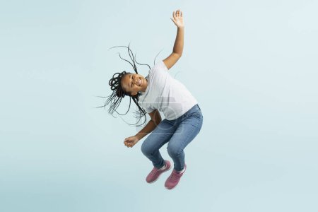 Foto de Hermosa chica afroamericana con peinado elegante en ropa casual, saltando, aislado sobre fondo azul, espacio de copia. El niño se divierte. Concepto de infancia - Imagen libre de derechos