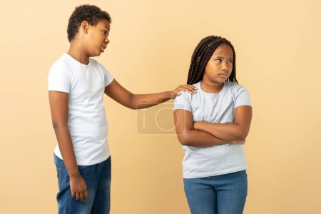 Photo for Portrait of attractive African American girl and boy, little brother apologizing to his little sister, supporting her isolated on beige background. ?oncept of family, relationships - Royalty Free Image