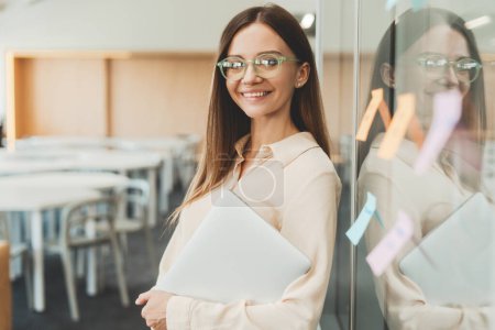 Photo for Young beautiful woman wearing stylish eyeglasses holding laptop using sticky notes, agile methodology for productivity working in modern office. Scrum master planning strategy - Royalty Free Image