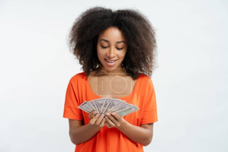Foto de Retrato de una hermosa mujer afroamericana sonriente con el pelo rizado usando ropa casual sosteniendo dinero, en efectivo aislado sobre fondo blanco. Concepto de inversión, publicidad - Imagen libre de derechos