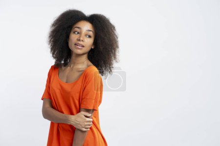 Foto de Retrato de modelo afroamericano auténtico con pelo rizado con camiseta naranja mirando hacia otro lado posando aislado sobre fondo blanco, espacio de copia. Concepto de publicidad - Imagen libre de derechos