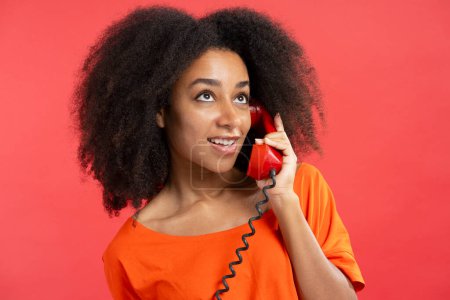 Photo for Beautiful authentic African American woman holding red handset, call looking away isolated on red background, closeup. Communication concept - Royalty Free Image