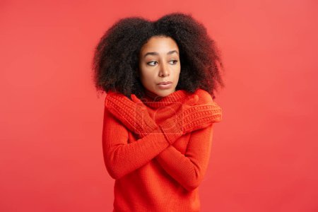 Photo for Portrait of upset beautiful African American woman with curly hair wearing red gloves looking away isolated on red background. Winter concept - Royalty Free Image