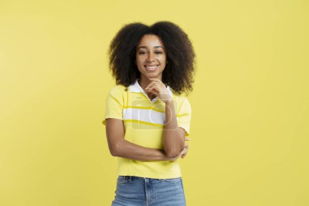 Téléchargez les photos : Belle femme afro-américaine positive portant une tenue décontractée élégante regardant la caméra isolée sur fond jaune. Concept d'entreprise prospère - en image libre de droit