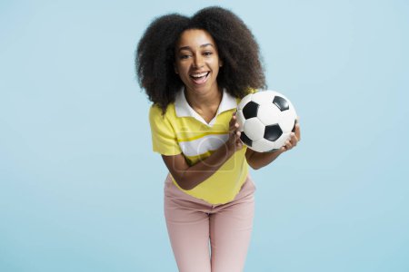 Photo for Smiling, beautiful African American woman holding soccer ball, wearing casual clothes, looking at camera isolated on blue background. Playing football concept - Royalty Free Image