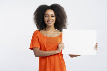 Téléchargez les photos : Portrait de belles femmes afro-américaines souriantes portant un t-shirt orange tenant une affiche vide ou une bannière isolée sur fond blanc, maquette. Concept de publicité - en image libre de droit