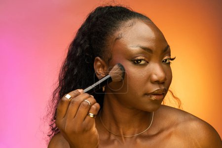 Téléchargez les photos : Jolie jeune femme utilisant un pinceau cosmétique pour appliquer un maquillage décoratif sur son visage, posant en studio. Concept beauté et cosmétique - en image libre de droit