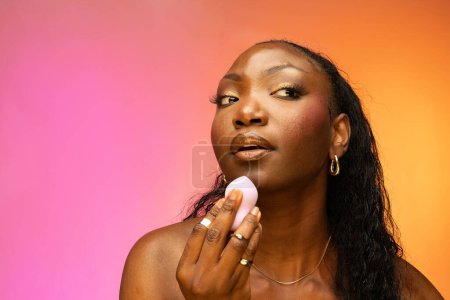 Photo for African American woman holding makeup egg sponge, powdering, making modern daily make-up, isolated on colorful background. Skin care and beauty concept - Royalty Free Image