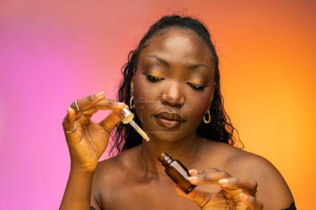 Foto de Primer plano de bastante afroamericana hembra sosteniendo suero para la cara, aislado sobre fondo colorido en el estudio. Concepto de cuidado facial - Imagen libre de derechos