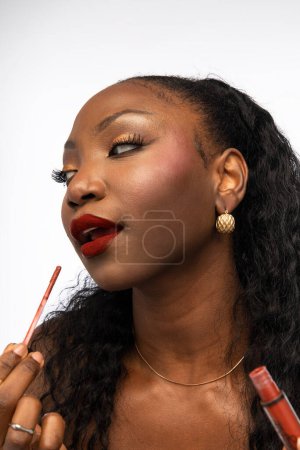 Téléchargez les photos : Gros plan de femme afro-américaine appliquant du brillant à lèvres avec applicateur, posant en studio, isolée sur fond blanc. Concept de beauté - en image libre de droit