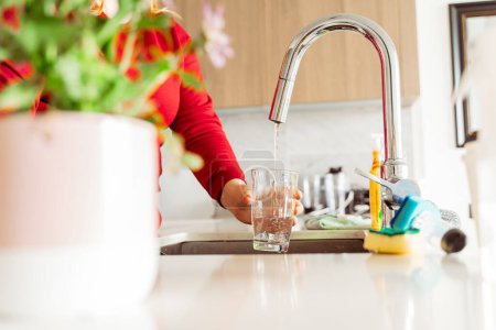 Photo for Woman pouring tap water into glass in stylish kitchen in apartment at home, selective focus. Health care concept - Royalty Free Image