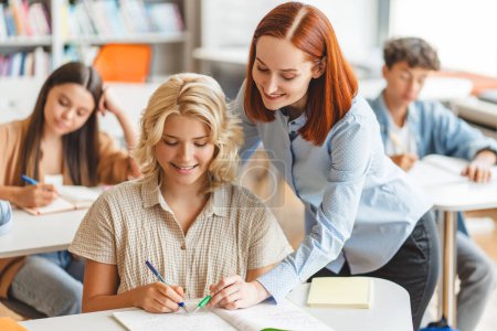 Photo for Young smiling teacher or tutor having lesson, explaining something, studying, learning language with school children sitting in classroom. Education, back to school concept - Royalty Free Image