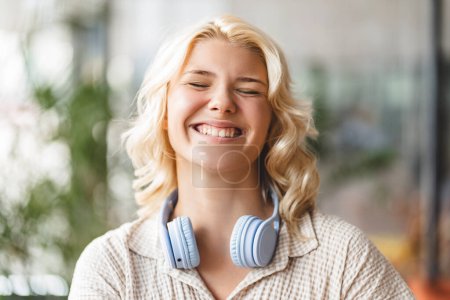 Foto de Auténtico retrato de niña linda y sonriente con los ojos cerrados usando auriculares inalámbricos. Tecnología, concepto de estilo de vida positivo - Imagen libre de derechos