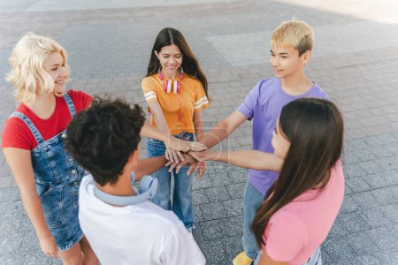 Photo for Stylish teenage boys and girls in colorful t shirts stacking hands together on the street, outdoors. Stylish hipsters college students friends meeting. Concept of team, friendship - Royalty Free Image
